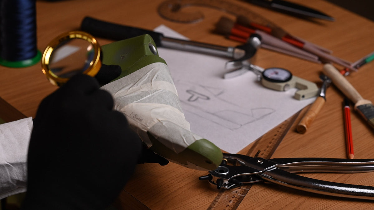 Gloved hand with a magnifier over a taped last, tools and pattern paper around it