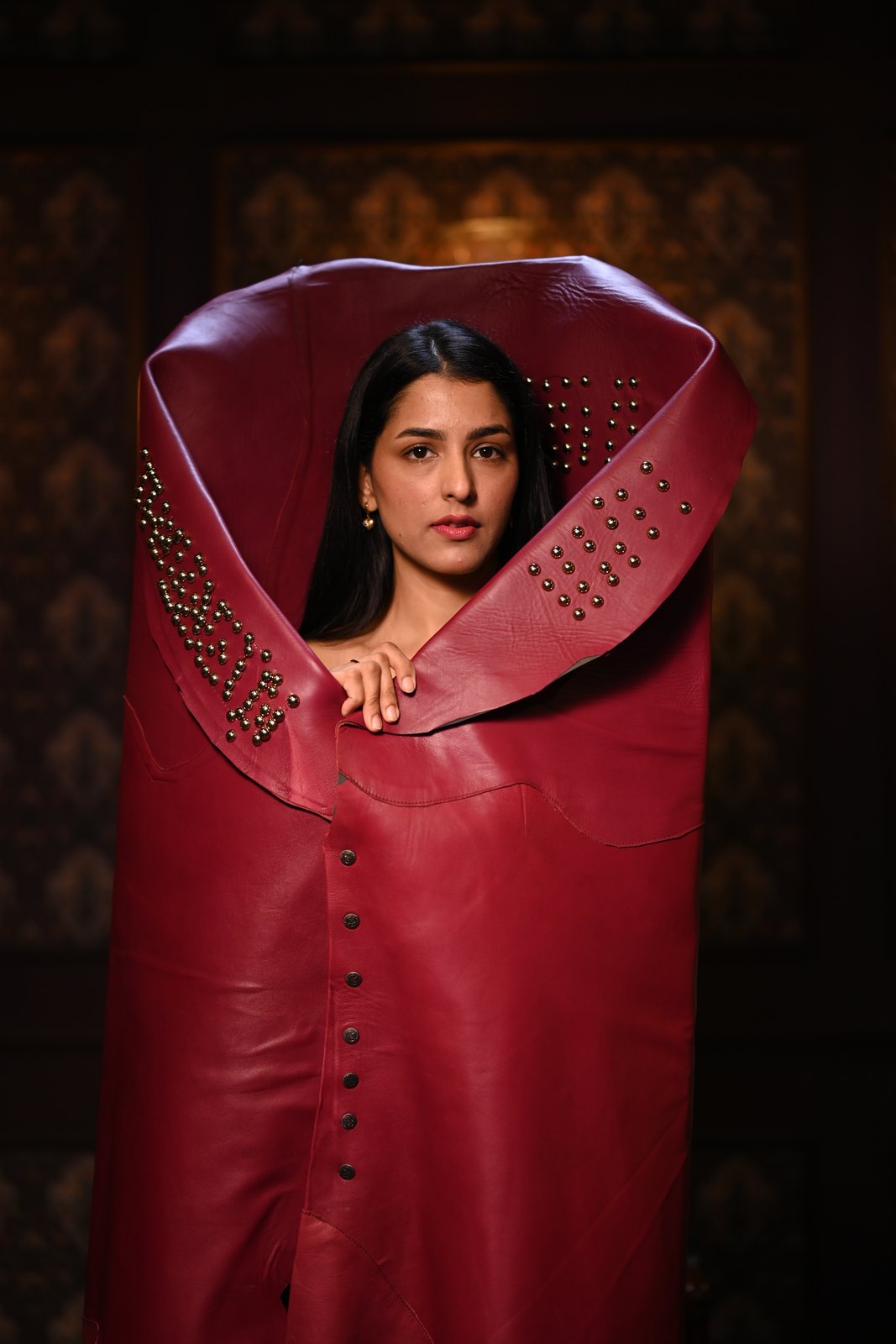 Woman framed by a tall studded burgundy leather wrap