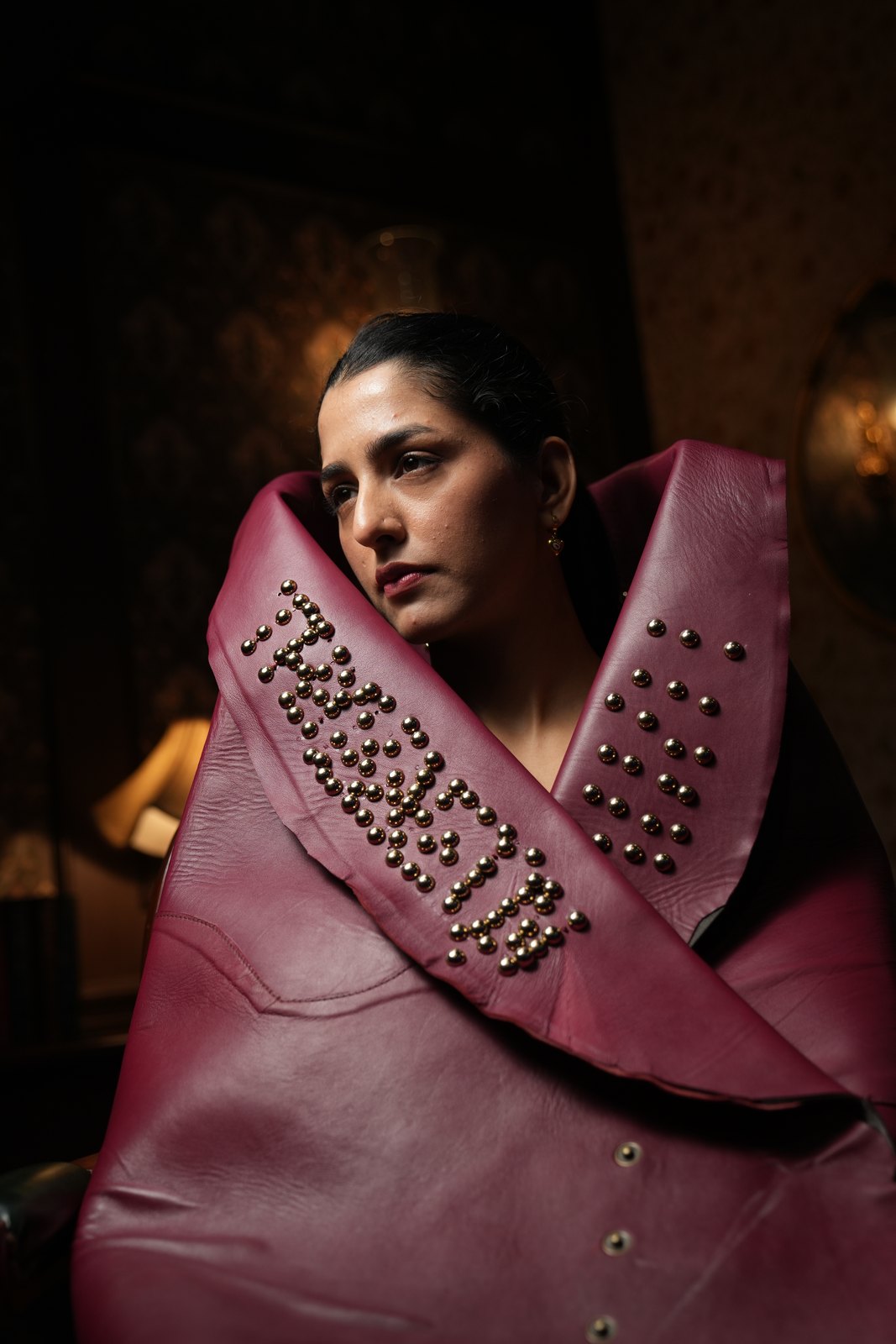 Woman in a studded burgundy leather wrap, gazing away in low light