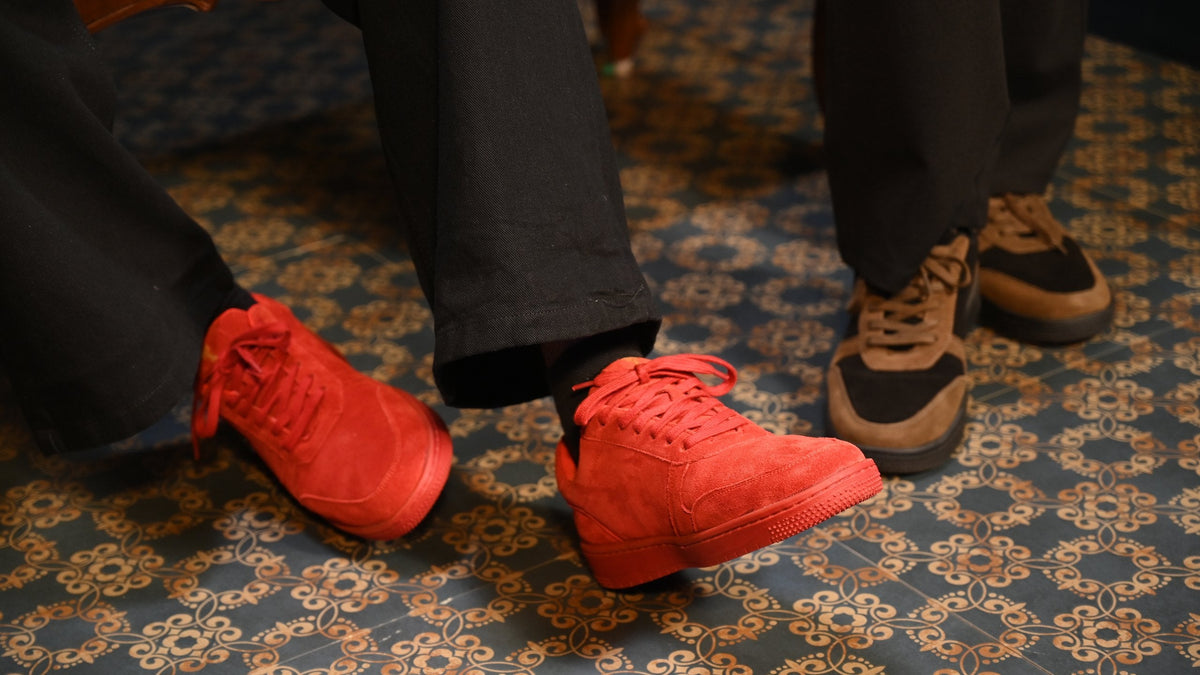 Feet in red suede and tan-and-black THYLACIN sneakers on a patterned carpet