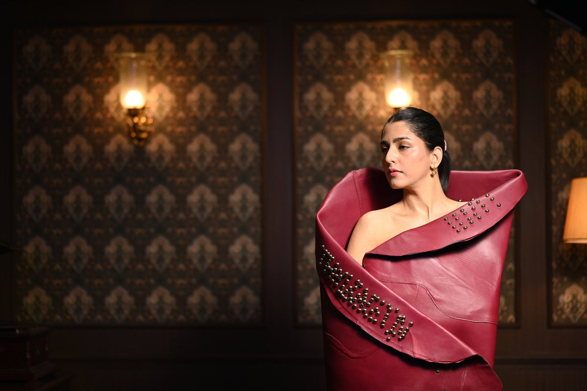 Woman wrapped in a studded burgundy leather hide, lamplit brocade walls behind