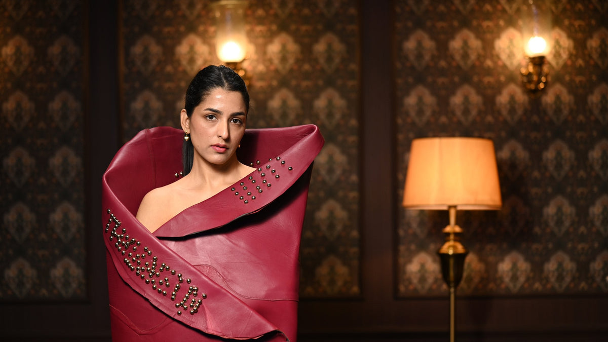 Woman in studded burgundy leather beside a lit floor lamp