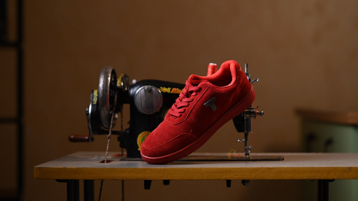 Red suede THYLACIN sneaker resting on a vintage sewing machine