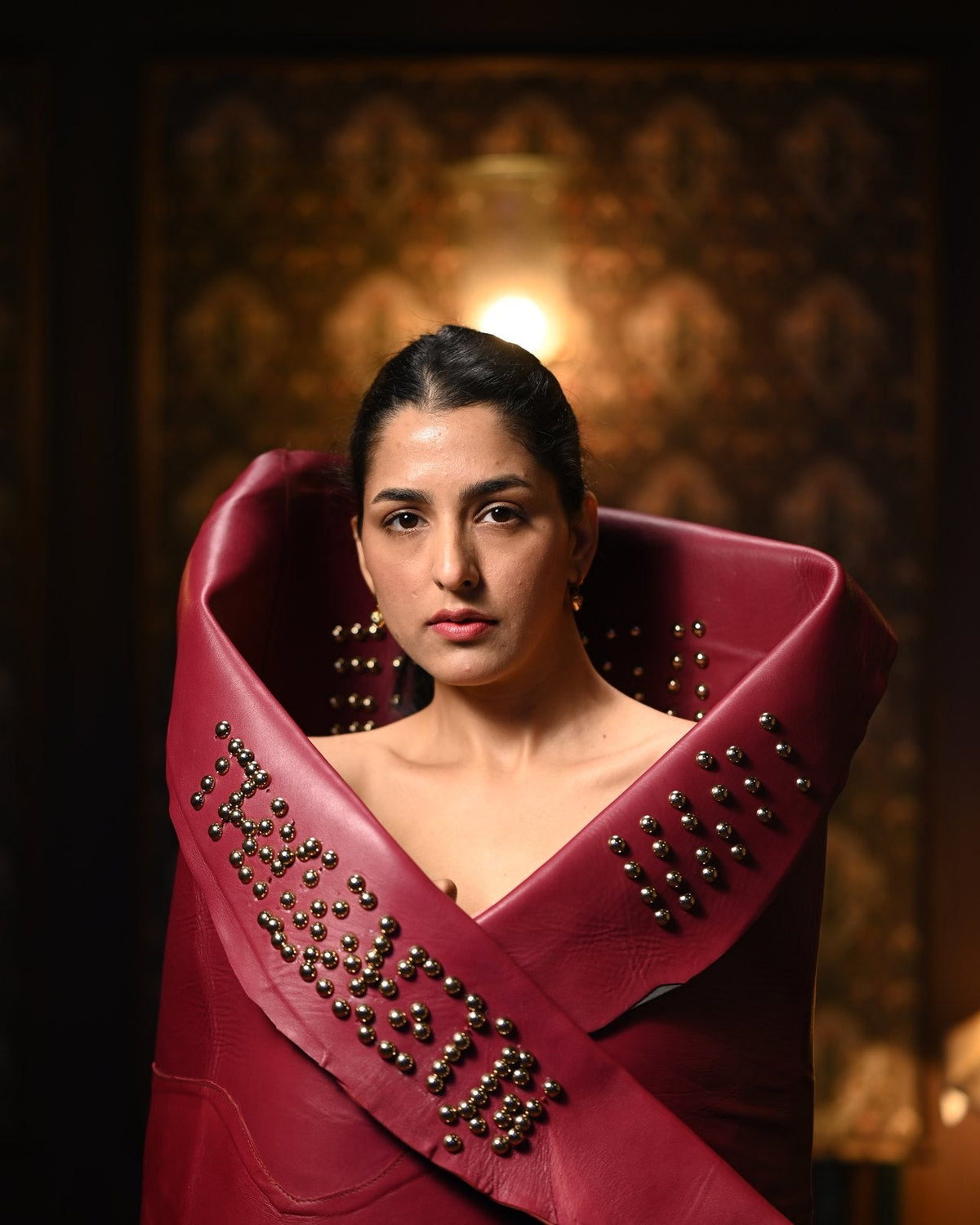 Woman in a studded burgundy leather wrap spelling THYLACIN, looking into the camera