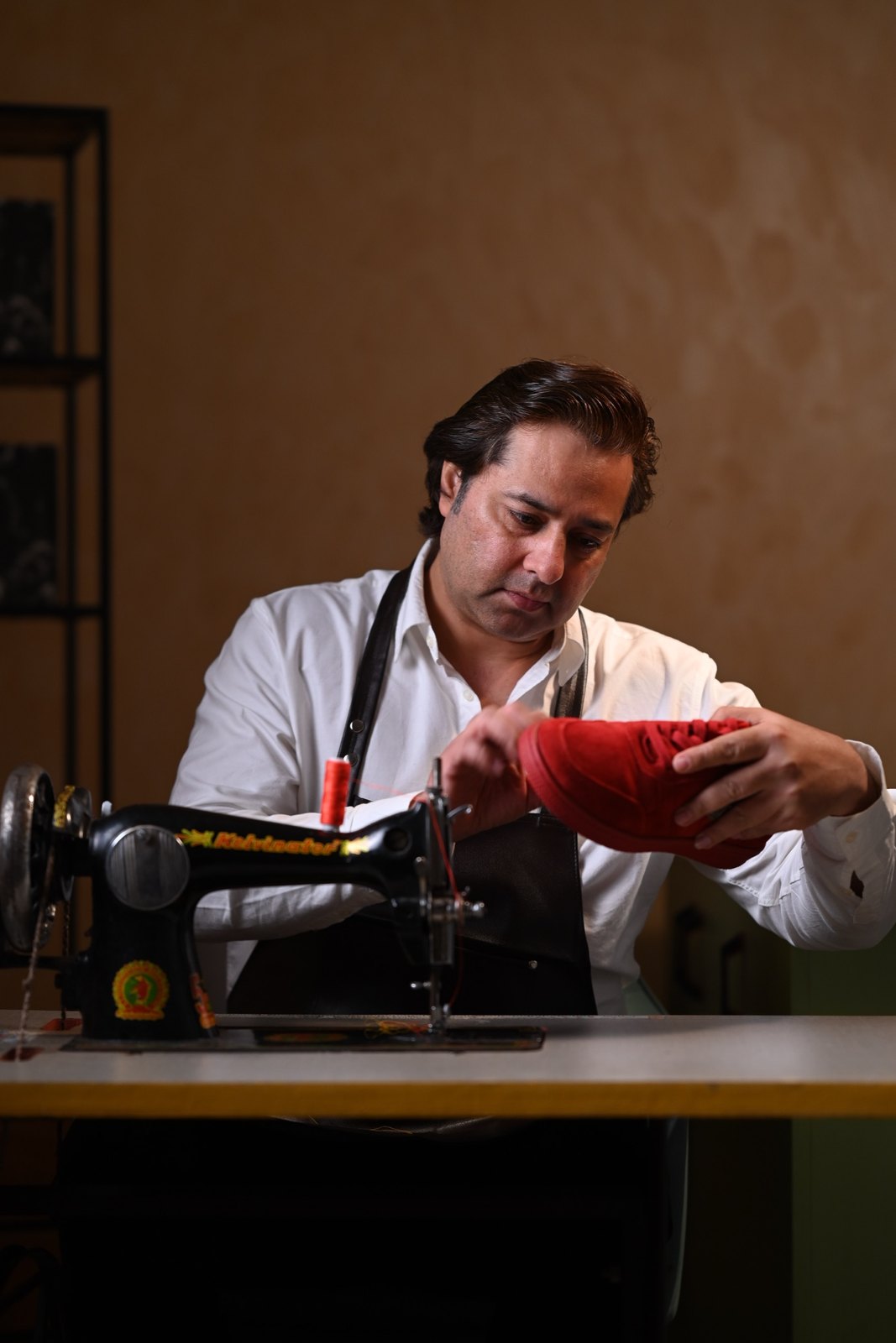 Shoemaker at a vintage sewing machine working on a red suede sneaker