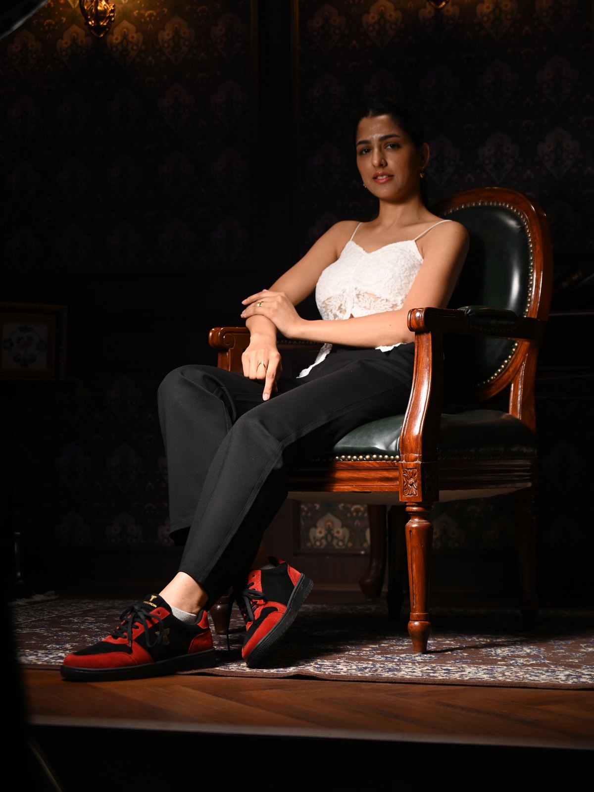 Woman in a white top seated in a leather armchair, wearing Ember Wolf red-and-black sneakers