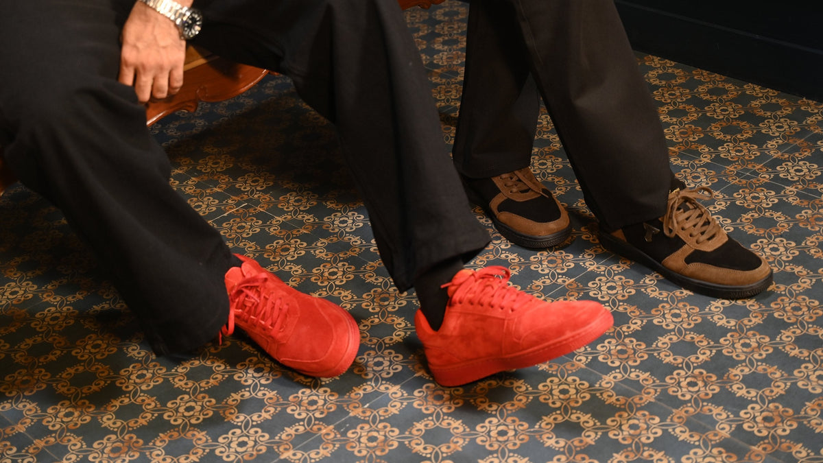 Two pairs of THYLACIN sneakers on a patterned carpet: red suede and tan-and-black