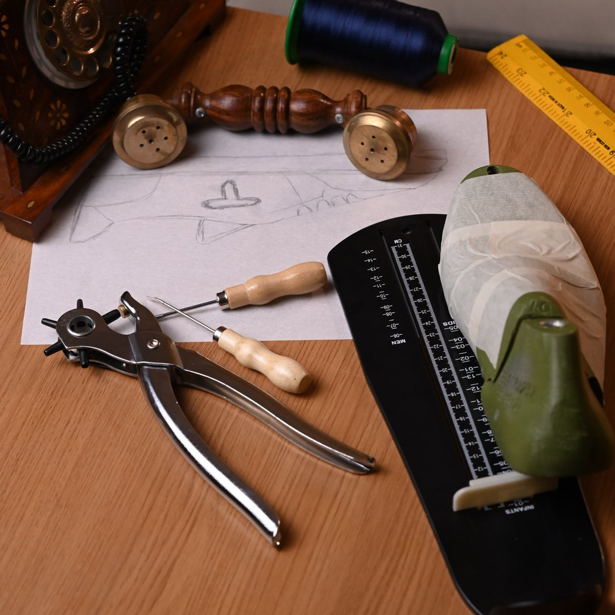Shoemaker's bench with pattern sketch, punch pliers, awl and a taped shoe last
